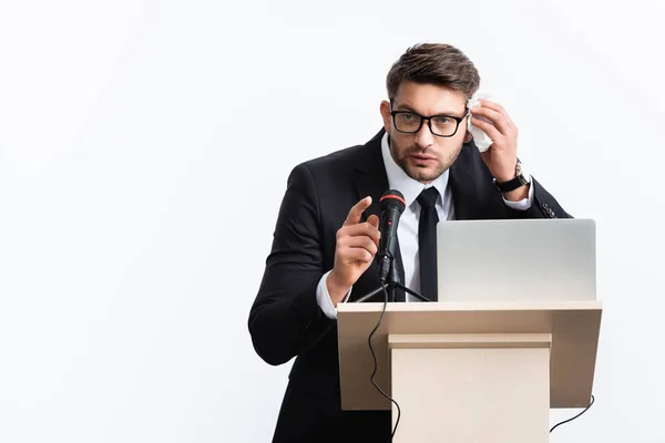 Hombre de negocios asustado en traje parado en tribuna del podio y hablando durante conferencia aislado en blanco - foto de stock