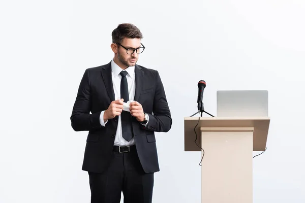 Asustado hombre de negocios en traje de pie cerca de tribuna podio durante conferencia aislado en blanco - foto de stock