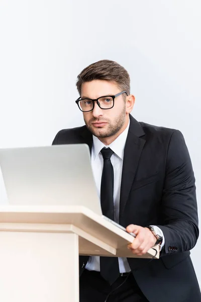 Scared businessman in suit standing at podium tribune and looking at camera during conference isolated on white — Stock Photo