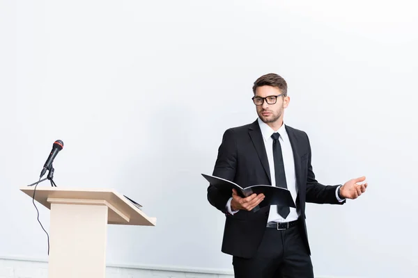 Geschäftsmann im Anzug hält Ordner in der Hand und schaut während einer Konferenz auf weißem Hintergrund weg — Stockfoto