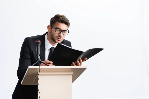 Hombre de negocios en traje de pie en tribuna podio y la celebración de carpeta durante la conferencia aislado en blanco - foto de stock