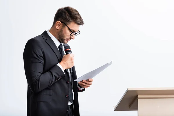 Geschäftsmann im Anzug hält Mikrofon in der Hand und schaut auf Papier während der Konferenz isoliert auf Weiß — Stockfoto