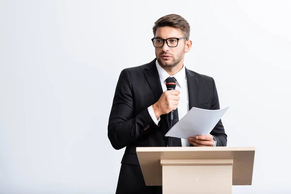 Hombre de negocios en traje de pie en el tribuno podio y hablando durante conferencia aislado en blanco - foto de stock