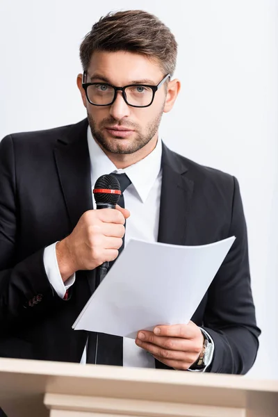 Empresario en traje sosteniendo papel y hablando durante conferencia aislado en blanco - foto de stock