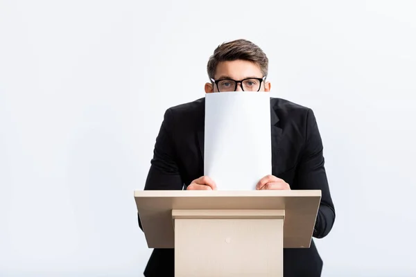 Homem de negócios assustado de terno em pé no tribuno pódio e rosto obscuro com papel durante conferência isolada em branco — Fotografia de Stock