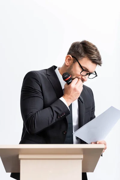 Scared businessman in suit standing at podium tribune and looking at paper during conference isolated on white — Stock Photo