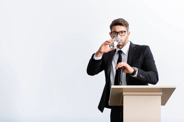 Scared businessman in suit standing at podium tribune and drinking water during conference isolated on white — Stock Photo