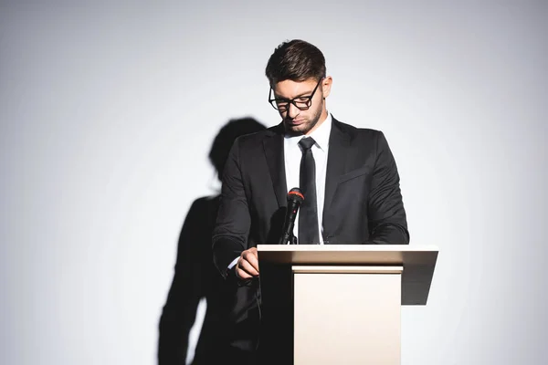Бизнесмен в костюме стоит на трибуне и смотрит вниз во время конференции на белом фоне — стоковое фото