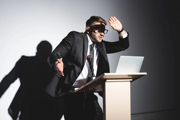 Homem de negócios assustado de terno em pé no tribuno pódio e rosto obscuro durante a conferência sobre fundo branco — Fotografia de Stock