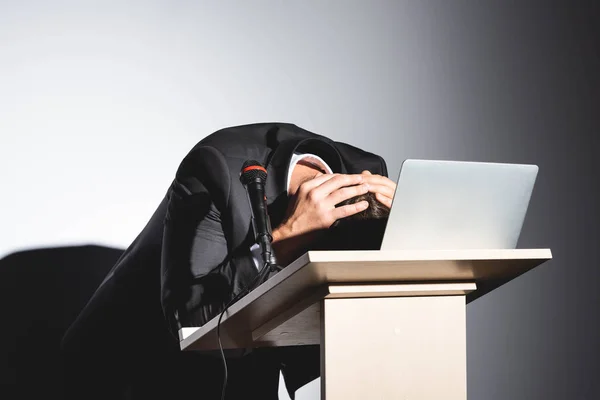 Scared businessman in suit standing at podium tribune and hiding behind laptop during conference on white background — Stock Photo