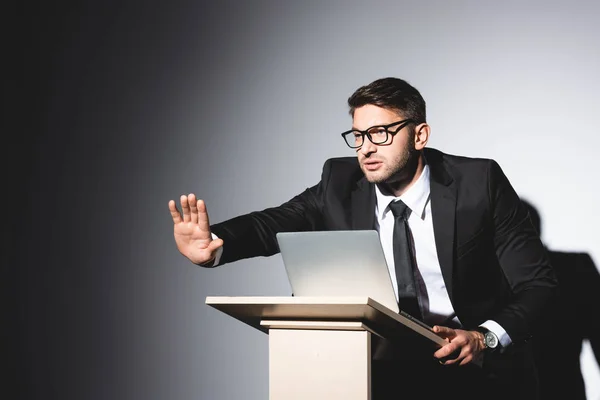 Scared businessman in suit with outstretched hand standing at podium tribune during conference on white background — Stock Photo