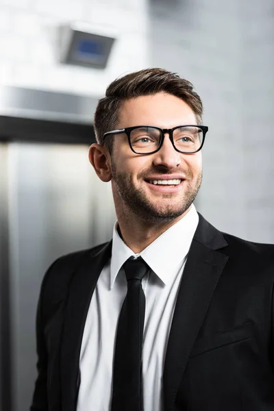 Sonriente hombre de negocios en ropa formal mirando hacia otro lado en la oficina - foto de stock