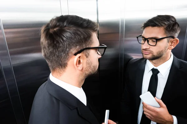 Vista de ángulo alto del hombre de negocios en traje mirando el espejo en ascensor - foto de stock