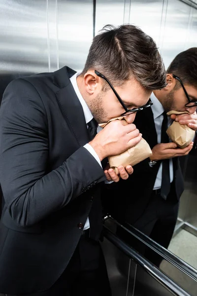 Scared businessman in suit with claustrophobia breathing in paper bag in elevator — Stock Photo