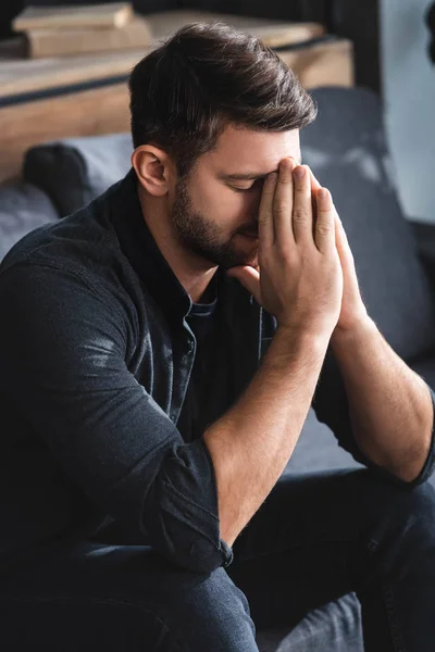 Hombre triste con los ojos cerrados que oscurecen la cara en el apartamento - foto de stock