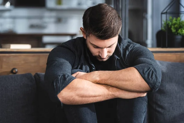 Uomo bello e triste in camicia che abbraccia le gambe in appartamento — Foto stock