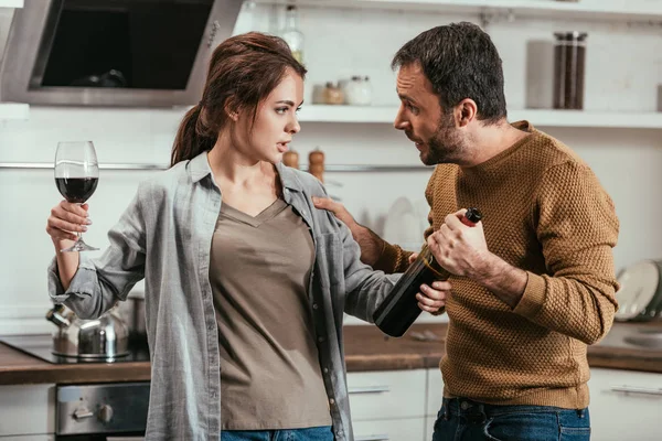 Woman holding wine and quarreling with husband on kitchen — Stock Photo