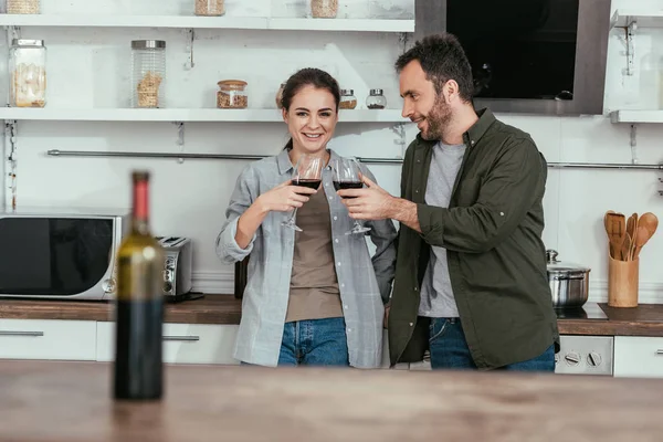 Foco selectivo de sonriente pareja tostadas con vino tinto en la cocina - foto de stock