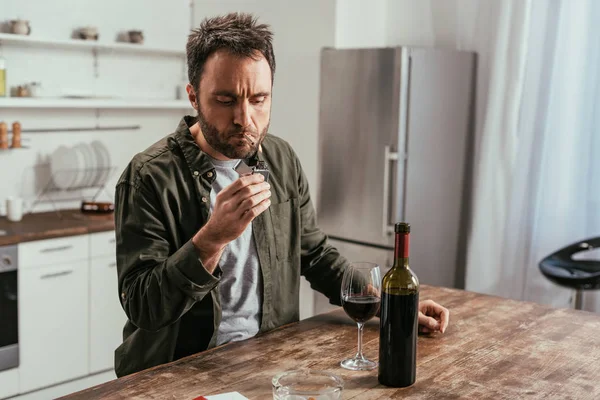 Alcohol adicto hombre iluminación cigarrillo al lado del vino en la mesa - foto de stock