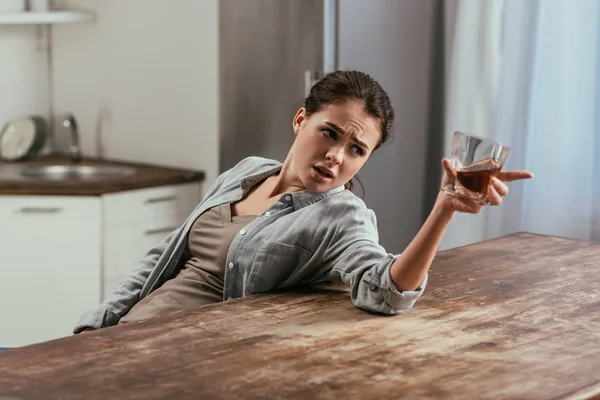 Mujer enojada con vaso de whisky hablando en algún lugar en la mesa de la cocina - foto de stock