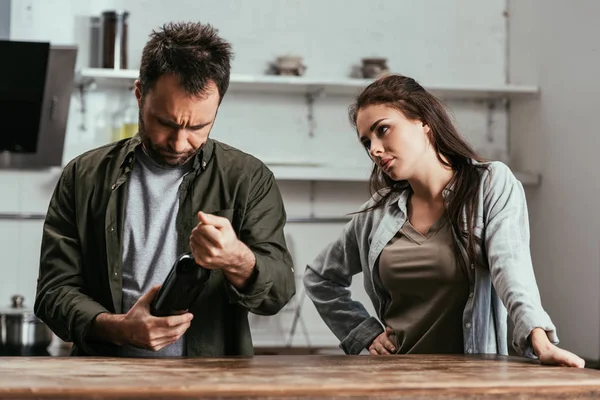 Donna seria guardando il marito con bottiglia di vino in cucina — Foto stock