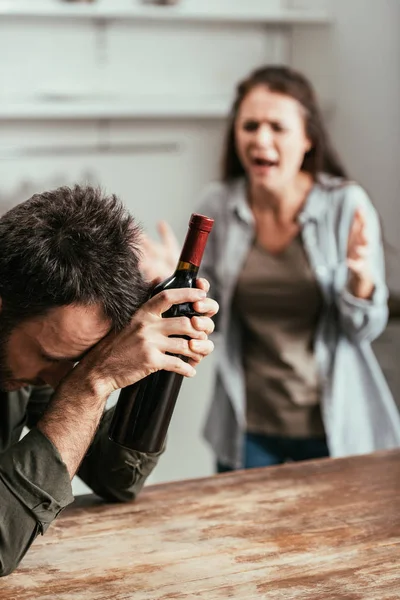 Foco seletivo do homem com garrafa de vinho e esposa gritando no fundo — Fotografia de Stock