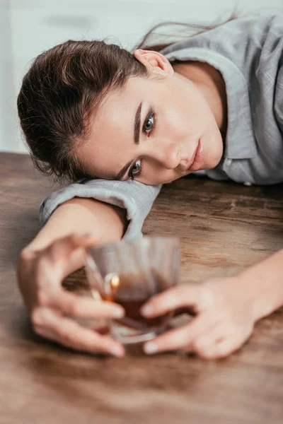 Selective focus of upset woman looking at whiskey glass at table — Stock Photo