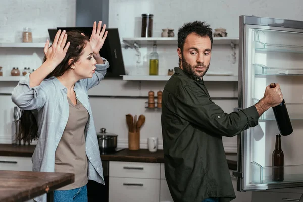 Woman quarreling while husband taking wine bottle from fridge — Stock Photo