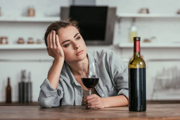 Mujer decepcionada sosteniendo copa de vino en la mesa de la cocina - foto de stock