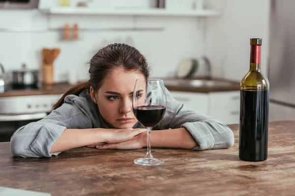 Mujer reflexiva mirando copa de vino en la mesa de la cocina - foto de stock