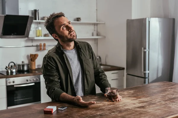 Mann hält Whiskey-Glas in der Hand und blickt auf Küchentisch — Stockfoto