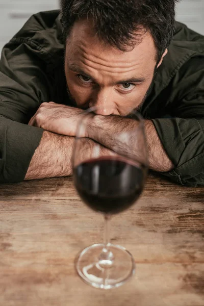 Selective focus of alcohol addicted man looking at wine glass on table — Stock Photo