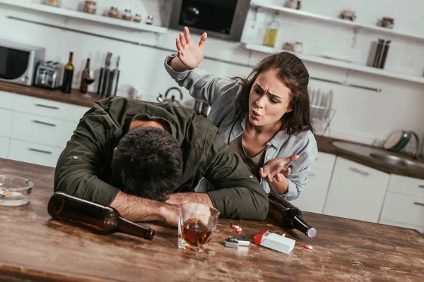 Злая женщина ссорится с пьяным мужем с алкогольной зависимостью на кухне — стоковое фото