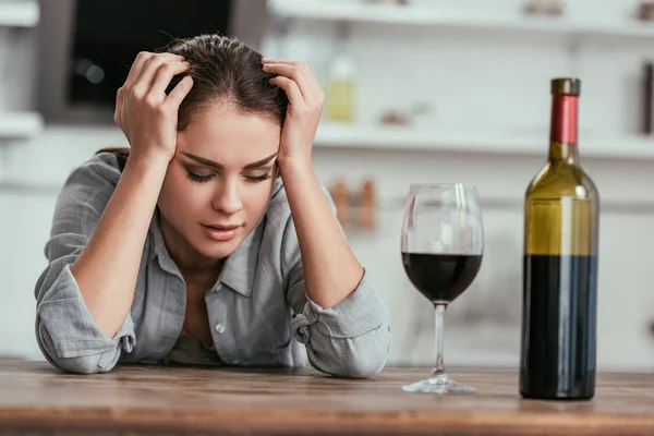 Selective focus of woman with alcohol addiction sitting beside wine on kitchen table — Stock Photo