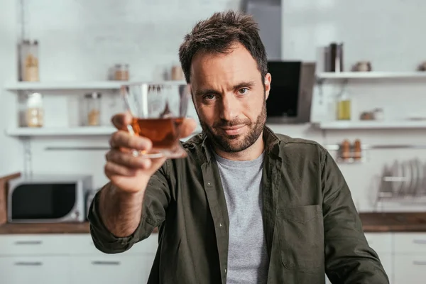 Selective focus of alcohol addicted man holding whiskey glass and looking at camera — Stock Photo