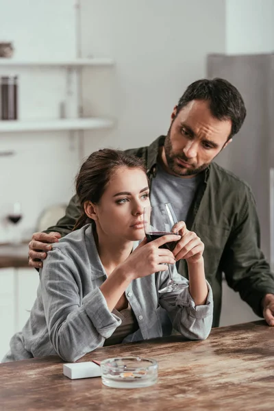 Mann schaut nachdenkliche Frau mit Weinglas in Küche an — Stockfoto