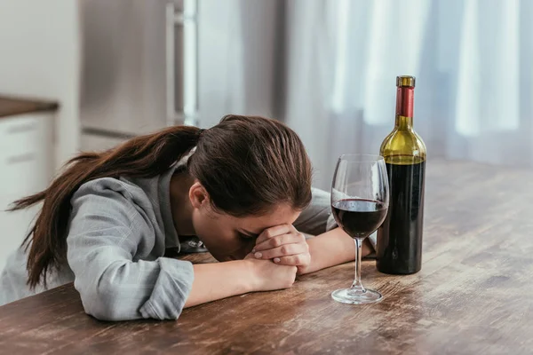 Mujer decepcionada al lado de copa de vino y botella en la mesa - foto de stock