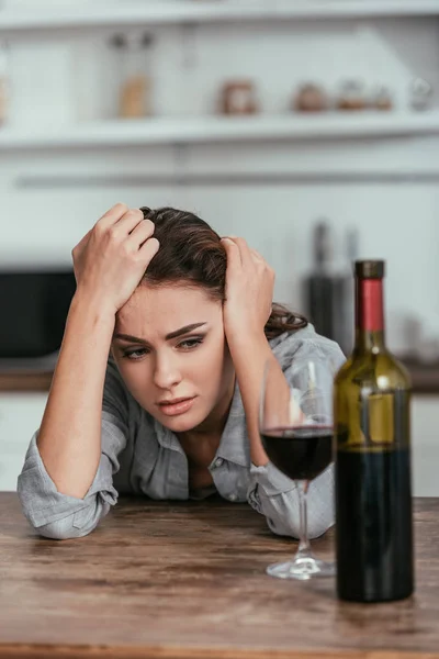 Selektiver Fokus einer depressiven Frau, die Wein auf dem Tisch betrachtet — Stockfoto