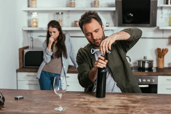 Enfoque selectivo del hombre abriendo botella de vino y esposa preocupada en la cocina - foto de stock