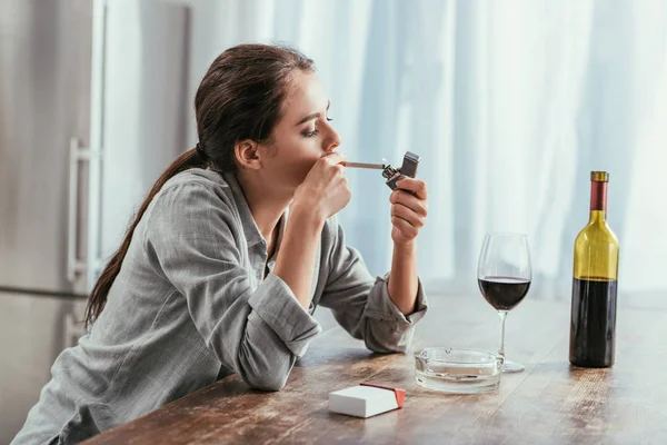 Mujer fumando cigarrillo con vino en la mesa de la cocina - foto de stock