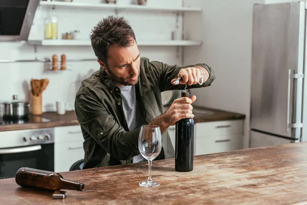 Hombre adicto al alcohol abriendo botella de vino en la cocina - foto de stock
