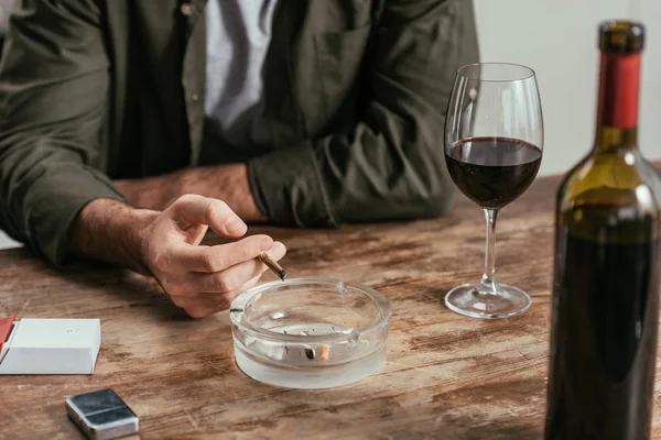 Vista recortada del hombre fumando cigarrillo junto a la copa de vino en la mesa - foto de stock