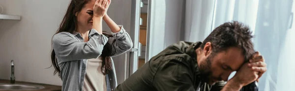 Selective focus of crying woman with alcohol addicted husband on kitchen, panoramic shot — Stock Photo