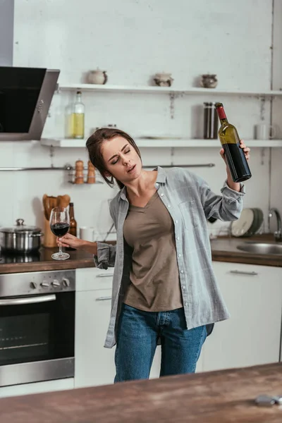 Femme avec de l'alcool dépendait tenant verre de vin et bouteille sur la cuisine — Photo de stock