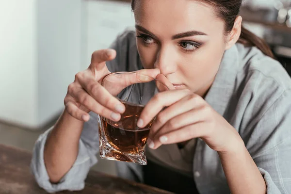 Vista de ángulo alto de la mujer sosteniendo vaso de whisky y mirando hacia otro lado - foto de stock