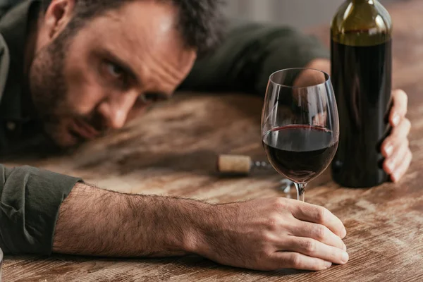 Focus selettivo dell'uomo sdraiato sulla tavola e in possesso di bicchiere di vino e bottiglia — Foto stock