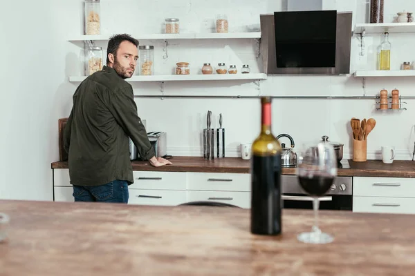 Enfoque selectivo del hombre pensativo mirando el vino en la mesa de la cocina - foto de stock