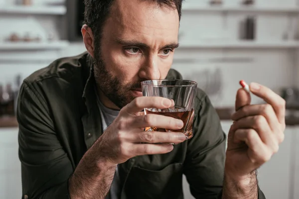 Selective focus of man with alcohol depended holding whiskey glass and pill — Stock Photo