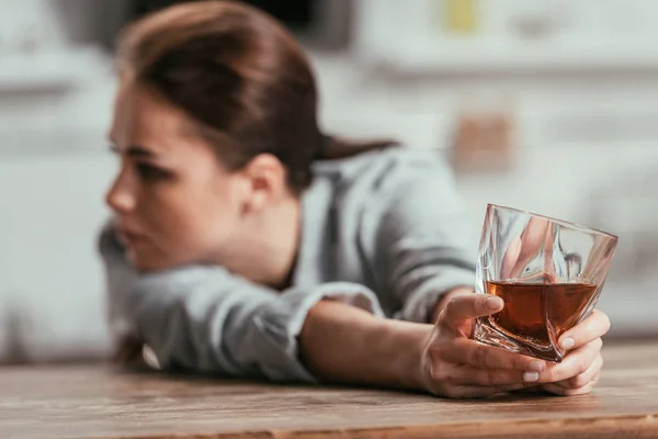 Enfoque selectivo de la mujer triste sosteniendo vaso de whisky en la mesa - foto de stock