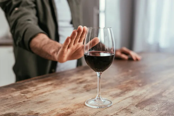 Vista recortada del hombre tirando de la mano a la copa de vino en la mesa - foto de stock